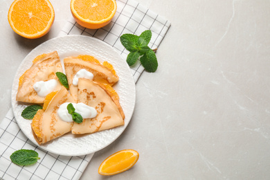 Photo of Delicious thin pancakes with oranges and cream on marble table, flat lay. Space for text