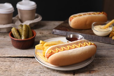 Delicious hot dog with ketchup, mustard and French fries on wooden table, closeup