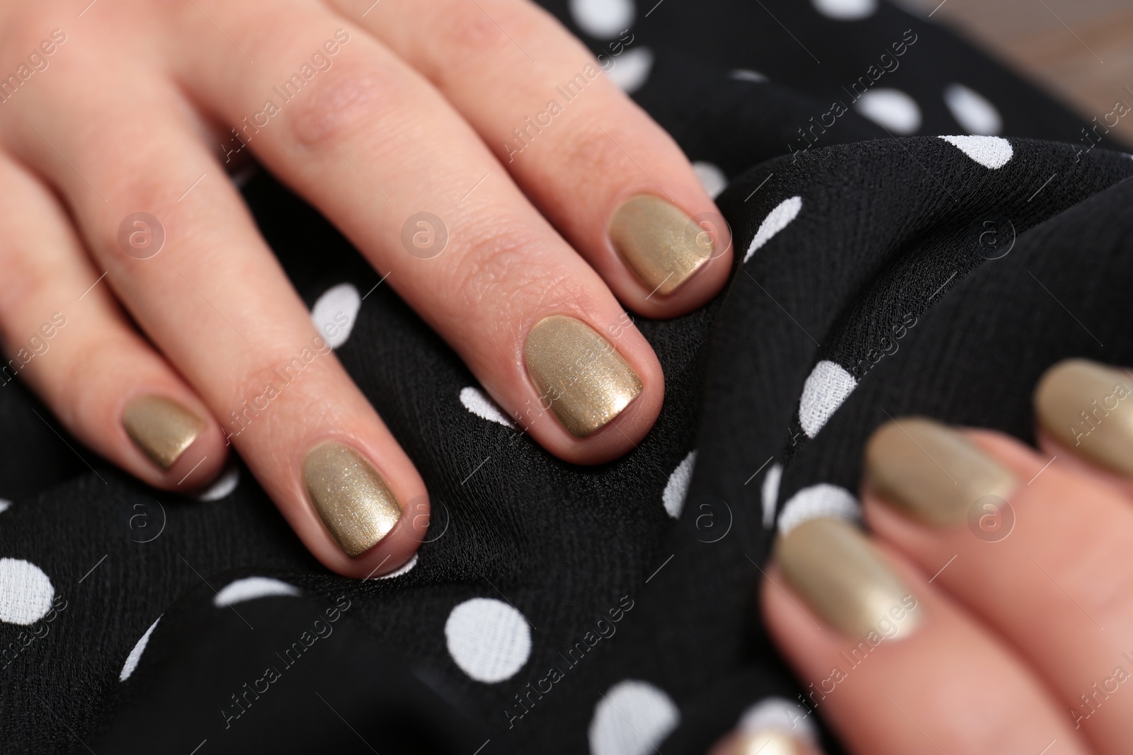 Photo of Woman with golden manicure holding fabric, closeup. Nail polish trends