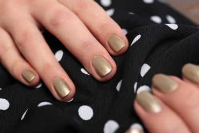 Woman with golden manicure holding fabric, closeup. Nail polish trends