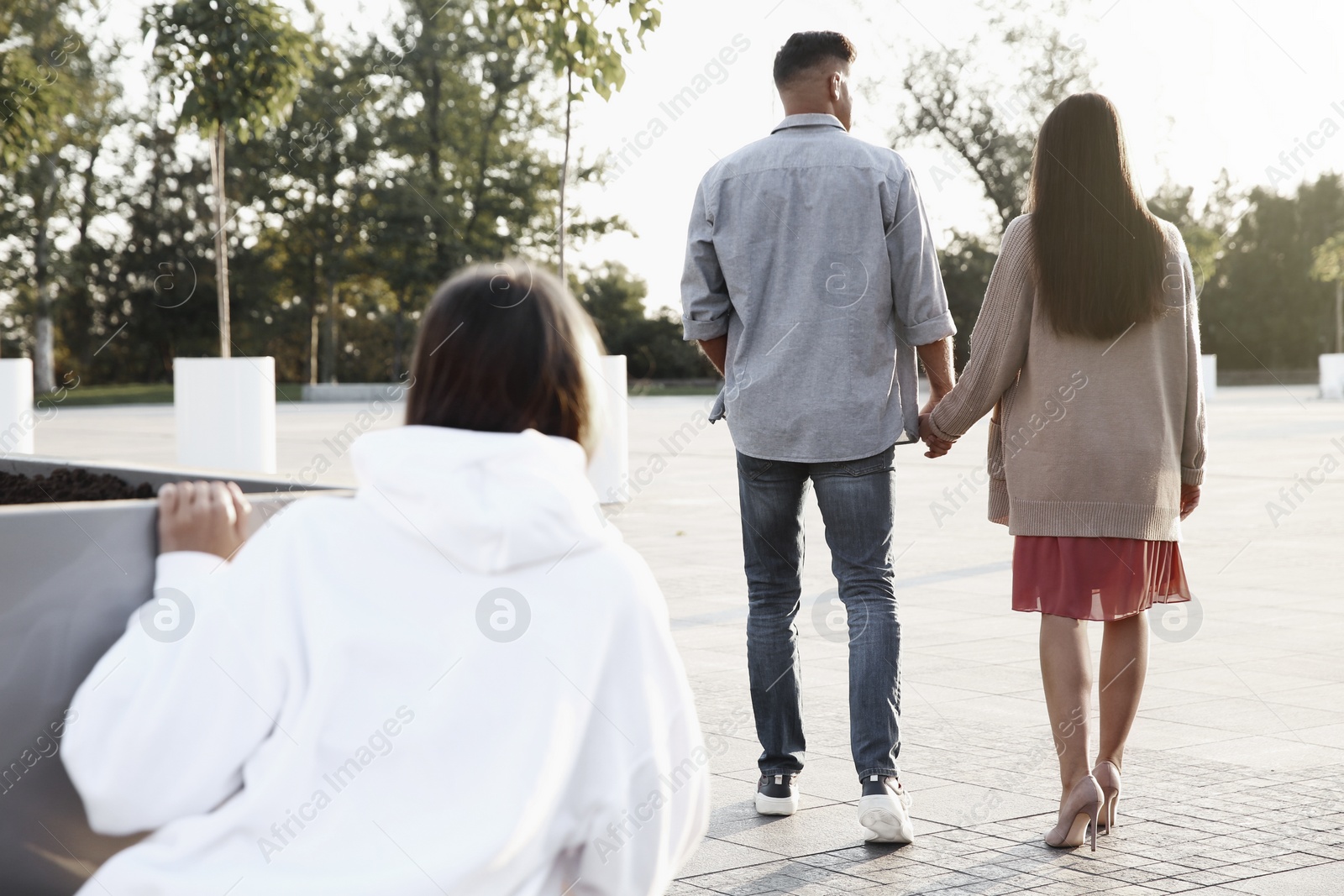 Image of Young woman spying on her boyfriend outdoors, back view. Cheating concept