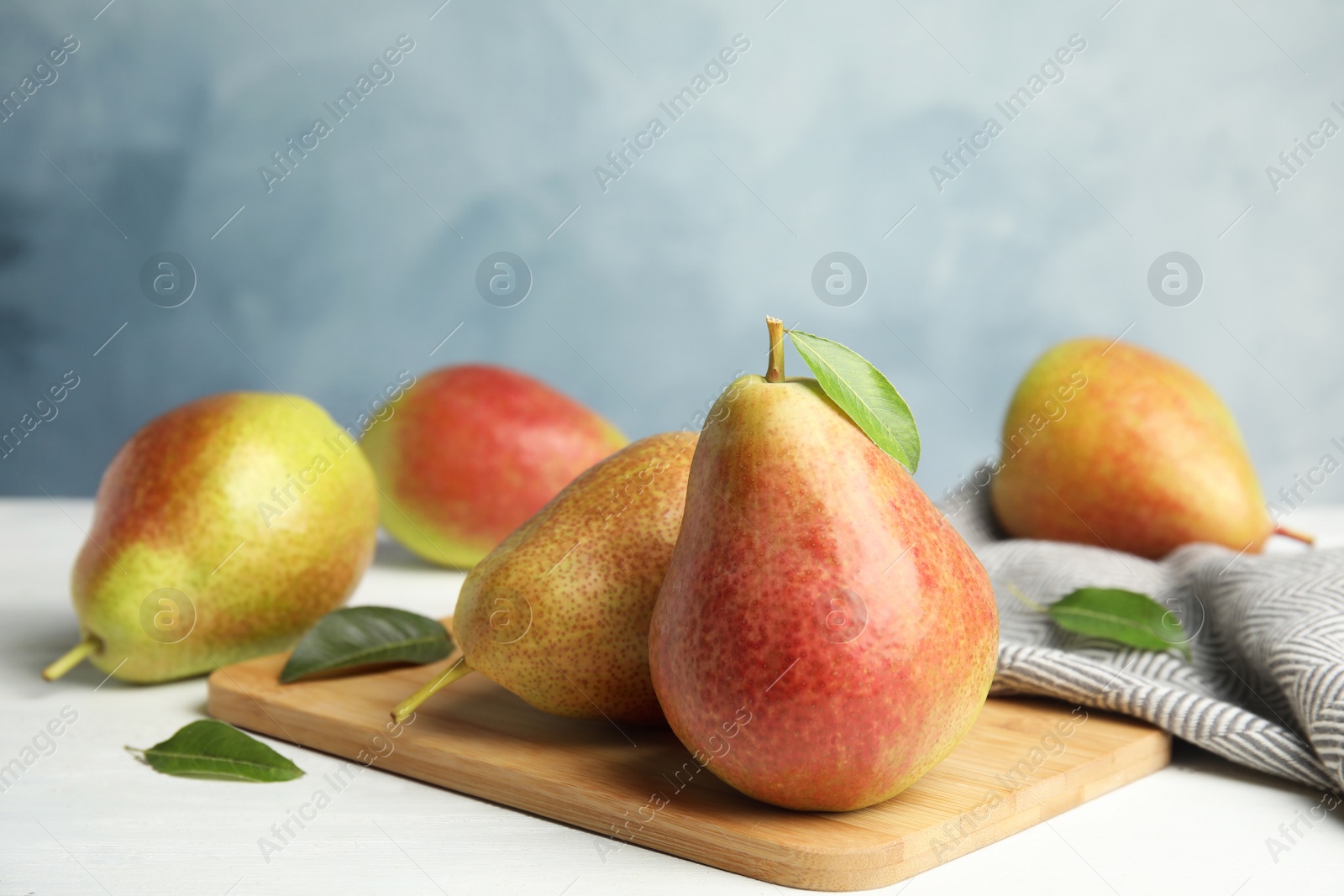 Photo of Ripe juicy pears on white wooden table against blue background. Space for text