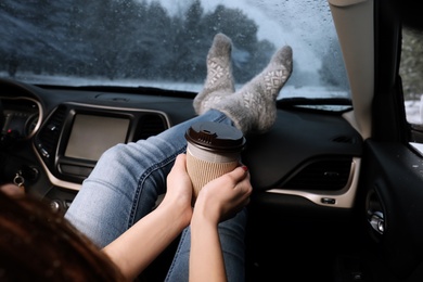 Photo of Young woman in warm socks with coffee resting inside car, closeup