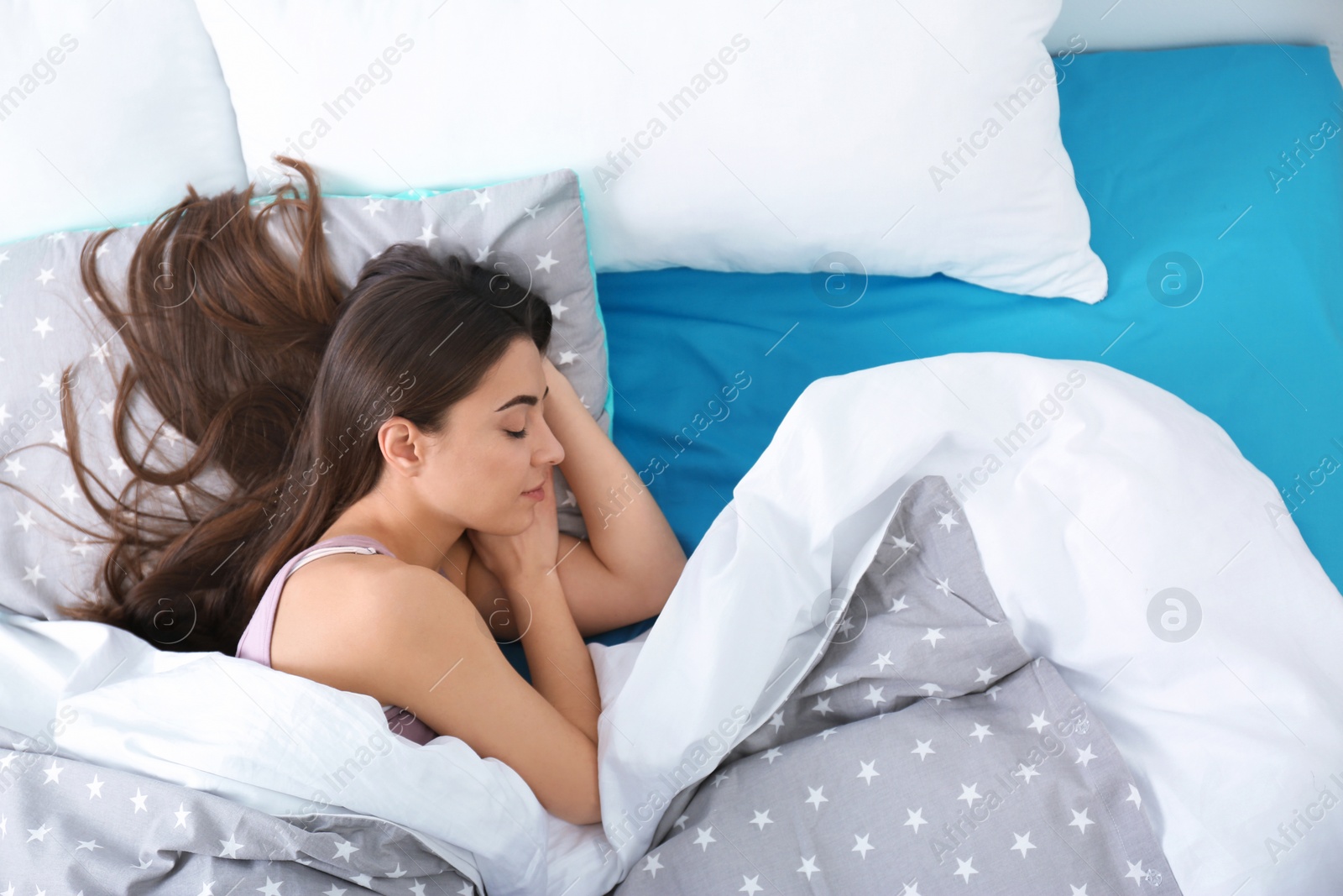 Photo of Young woman sleeping on soft pillow, top view. Bedtime