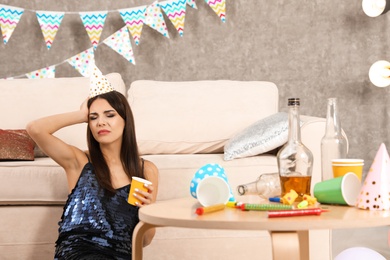 Photo of Young woman suffering from hangover in messy room after party