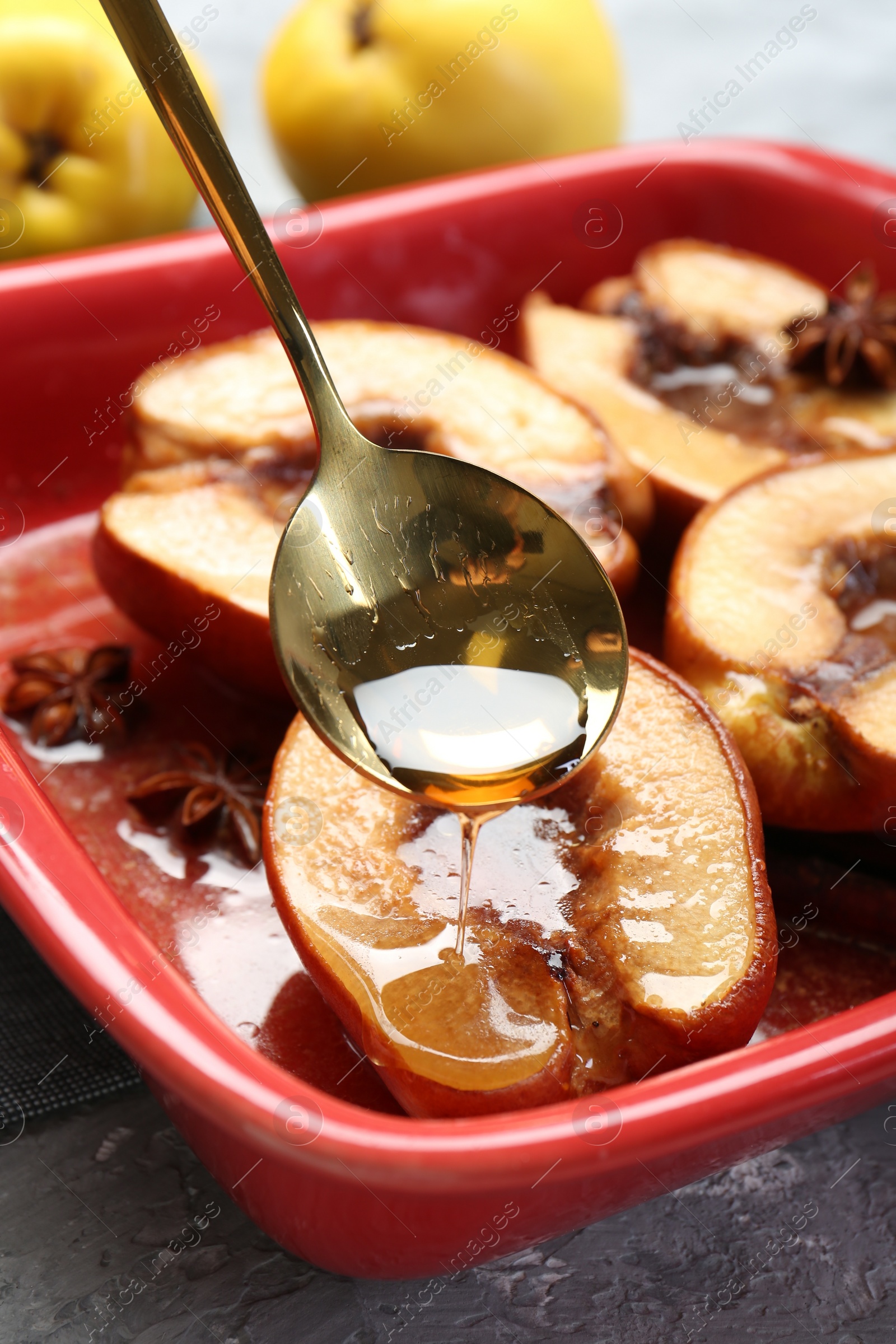Photo of Pouring tasty honey onto baked quinces in dish on grey textured table, closeup