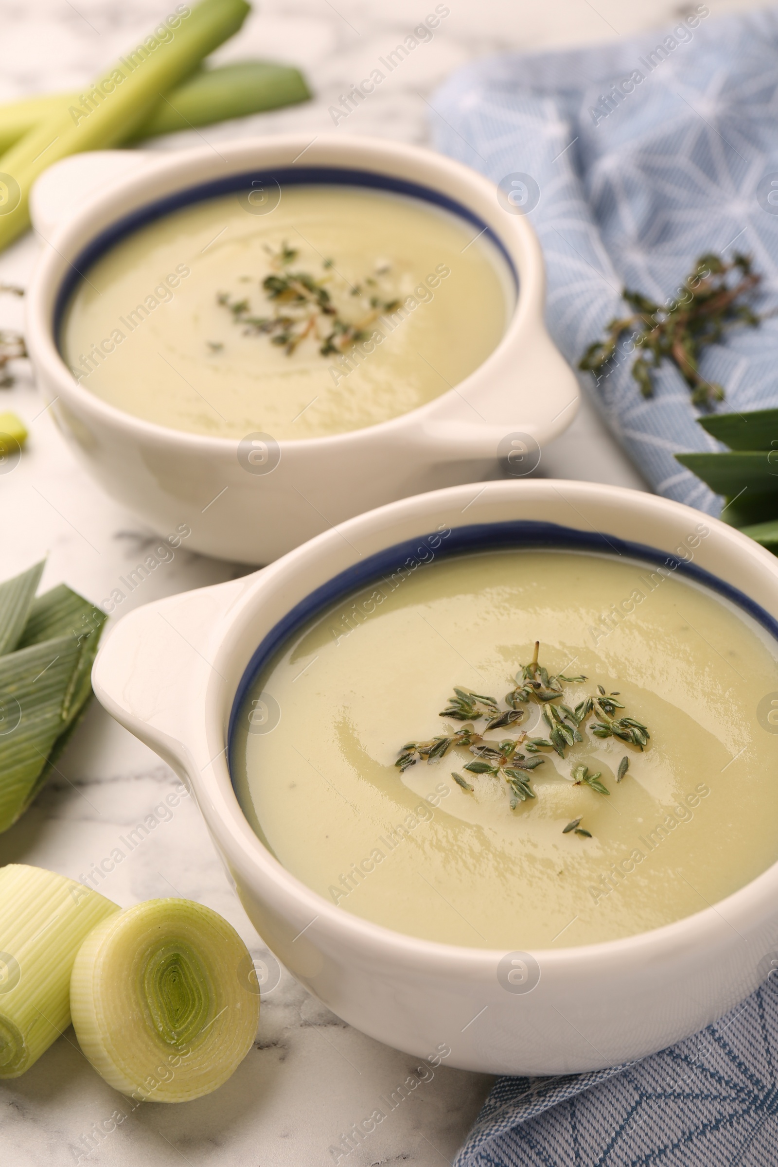 Photo of Tasty leek soup in bowls on white marble table