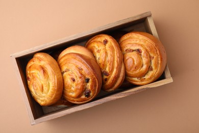 Photo of Delicious rolls with raisins in wooden box on beige table, top view. Sweet buns