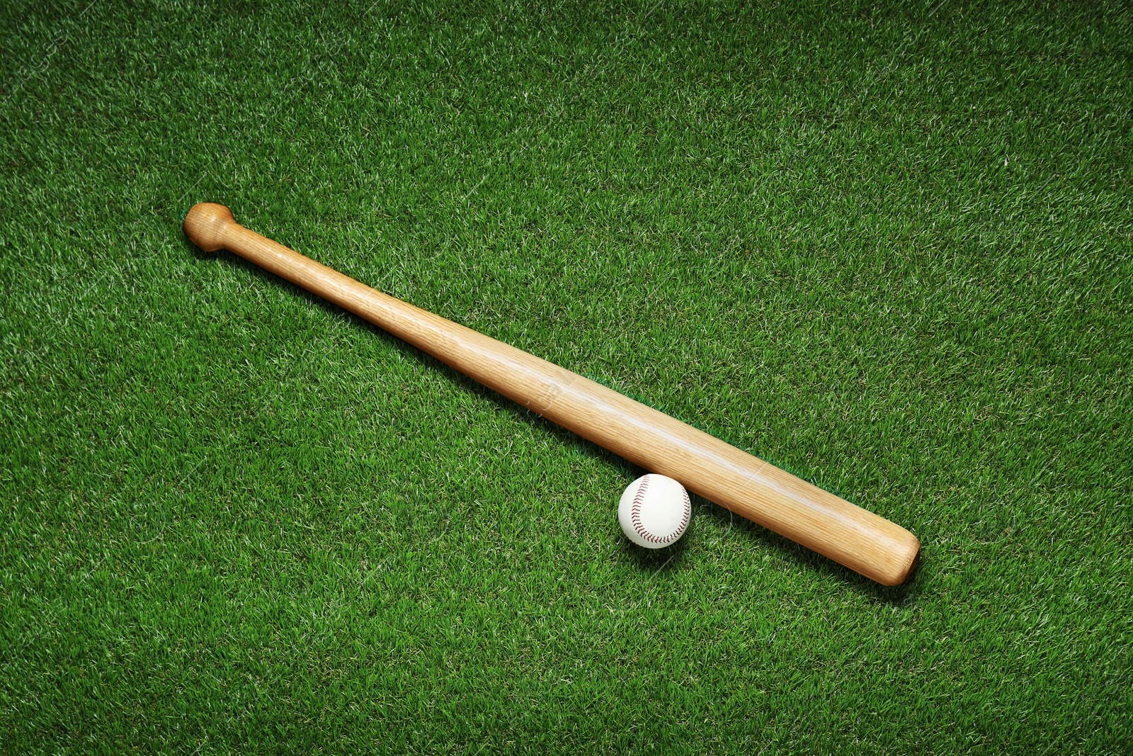 Photo of Wooden baseball bat and ball on green grass, flat lay. Sports equipment