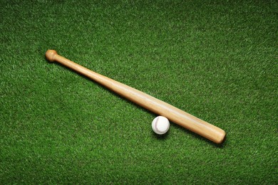 Photo of Wooden baseball bat and ball on green grass, flat lay. Sports equipment