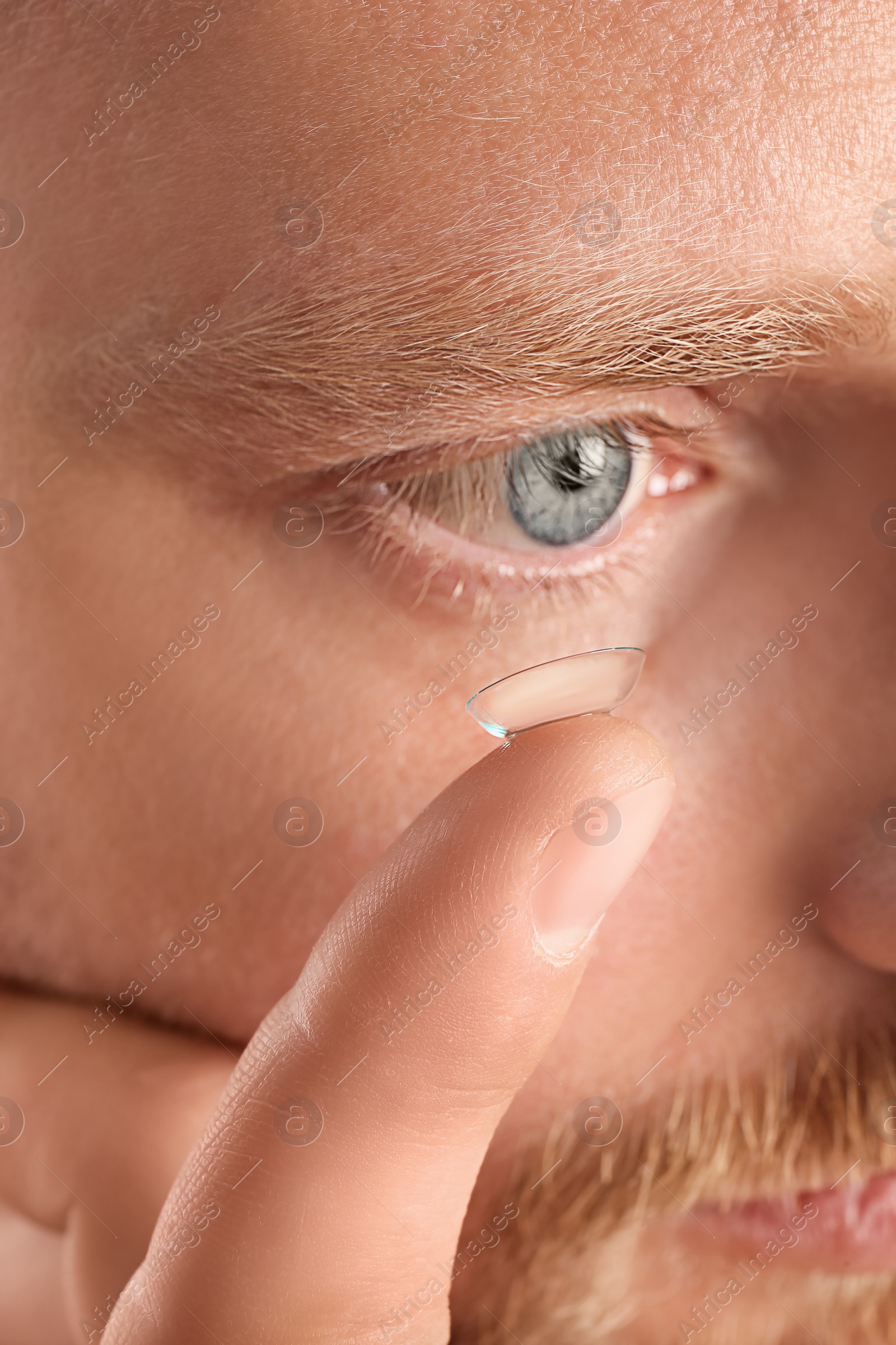 Photo of Young man putting contact lens into his eye, closeup