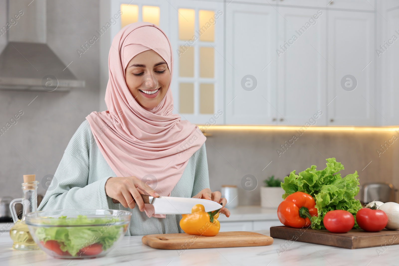 Photo of Muslim woman making delicious salad with vegetables at white table in kitchen. Space for text