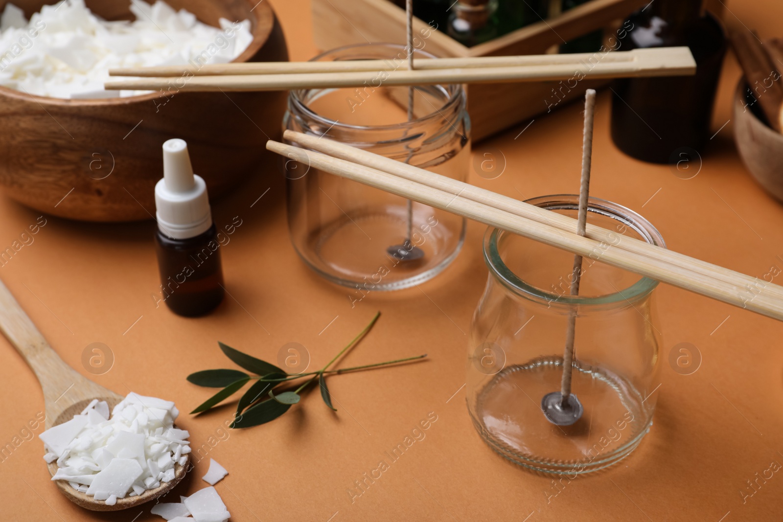 Photo of Glass jars with wicks, wax flakes and essential oil on brown background. Making homemade candles