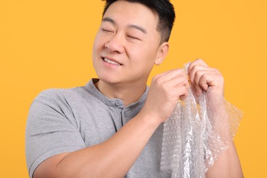 Happy asian man with bubble wrap on orange background