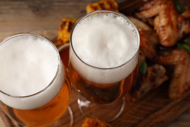 Photo of Glasses with beer and delicious baked chicken wings on table, closeup
