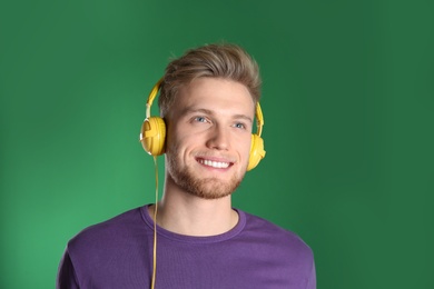 Handsome young man listening to music with headphones on color background