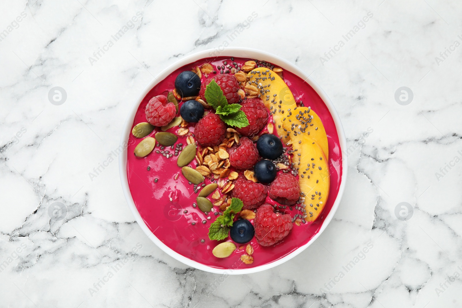 Photo of Delicious acai smoothie with granola and berries in dessert bowl on white marble table, top view