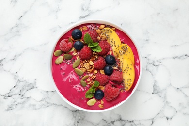 Photo of Delicious acai smoothie with granola and berries in dessert bowl on white marble table, top view