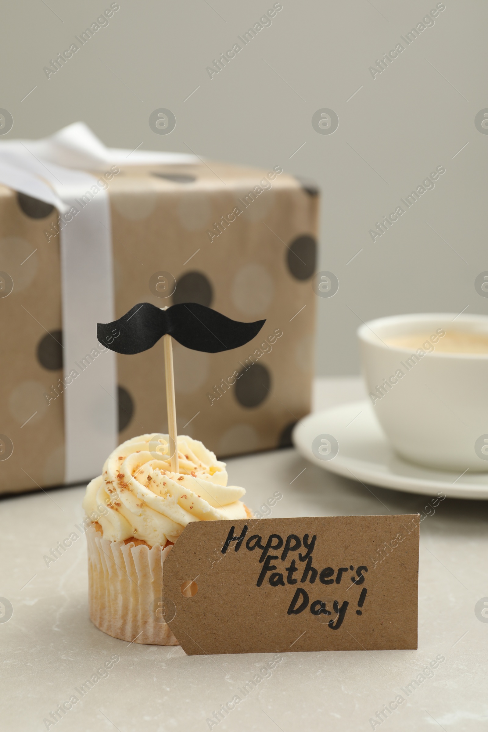 Photo of Card with phrase Happy Father's Day and delicious cupcake with mustache topper on light table