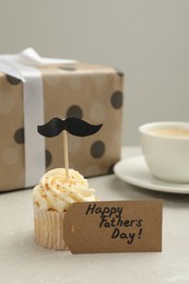 Card with phrase Happy Father's Day and delicious cupcake with mustache topper on light table