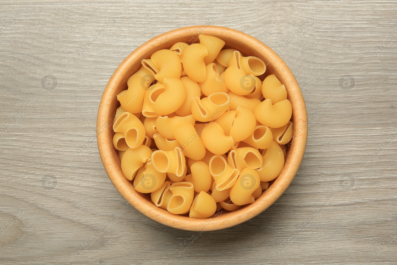 Photo of Raw macaroni pasta in bowl on light grey wooden table, top view