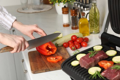 Photo of Woman cooking different products with electric grill at white wooden table in kitchen, closeup