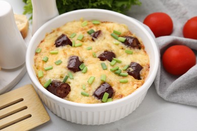 Photo of Tasty sausage casserole with green onions in baking dish served on white tiled table, closeup