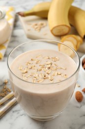 Photo of Glass of tasty banana smoothie with oatmeal on white marble table, closeup