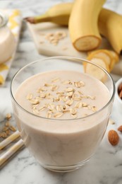 Glass of tasty banana smoothie with oatmeal on white marble table, closeup