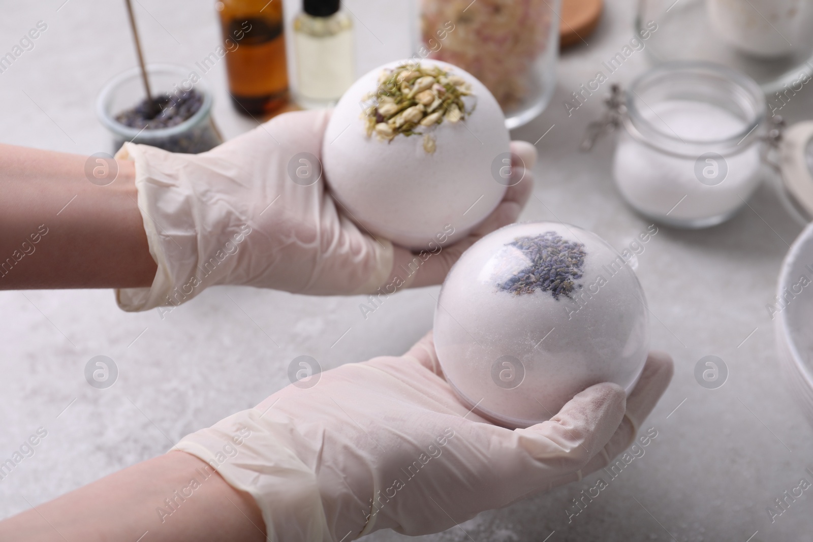 Photo of Woman in gloves with self made bath bombs at grey table, closeup