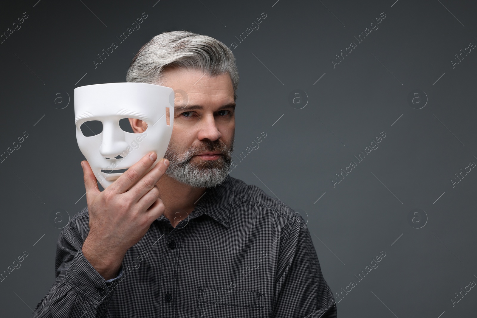 Photo of Multiple personality concept. Man with mask on dark grey background, space for text