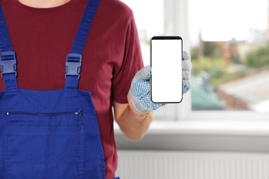 Professional repairman in uniform with phone indoors, closeup. Space for text
