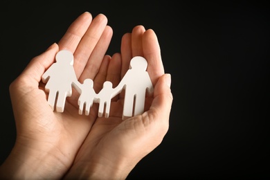 Photo of Woman holding figure of family in hands on black background, closeup. Space for text