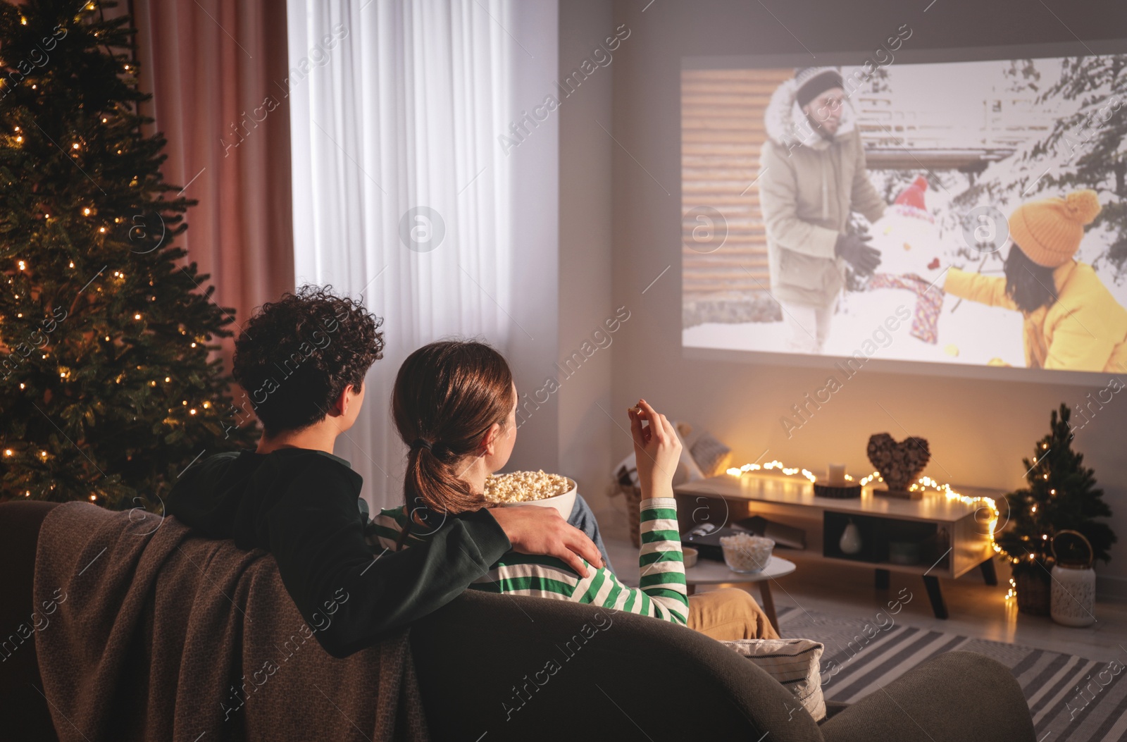 Photo of Couple watching romantic Christmas movie via video projector at home