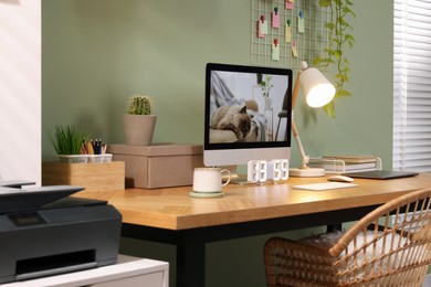 Stylish workplace with computer, laptop and lamp near olive wall at home