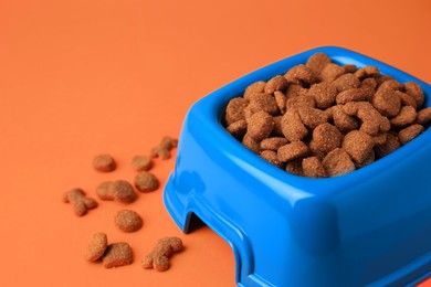Dry pet food in feeding bowl on orange background, closeup. Space for text