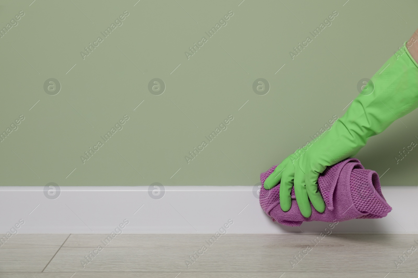 Photo of Woman in protective glove cleaning plinth with washcloth indoors, closeup. Space for text