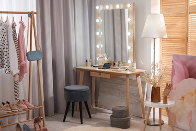 Makeup room. Stylish dressing table with mirror, chair and clothes rack indoors