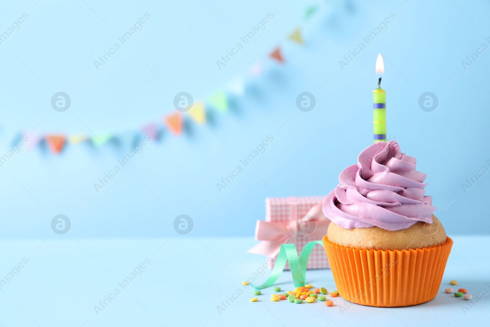 Photo of Birthday cupcake with burning candle and gift box on light blue table. Space for text