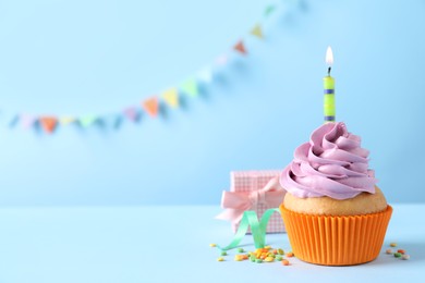 Photo of Birthday cupcake with burning candle and gift box on light blue table. Space for text