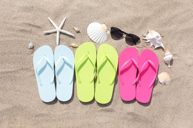 Stylish colorful flip flops, sunglasses, seashells and starfish on sand outdoors, flat lay