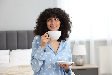 Beautiful young woman in stylish pyjama with cup of drink at home