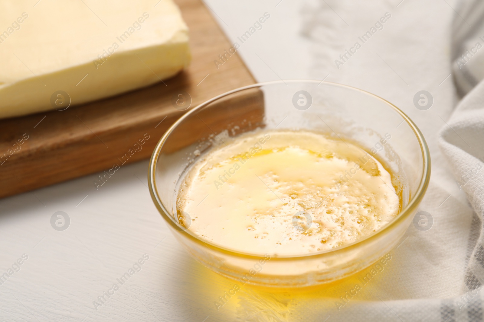 Photo of Melted butter in glass bowl on white wooden table, closeup