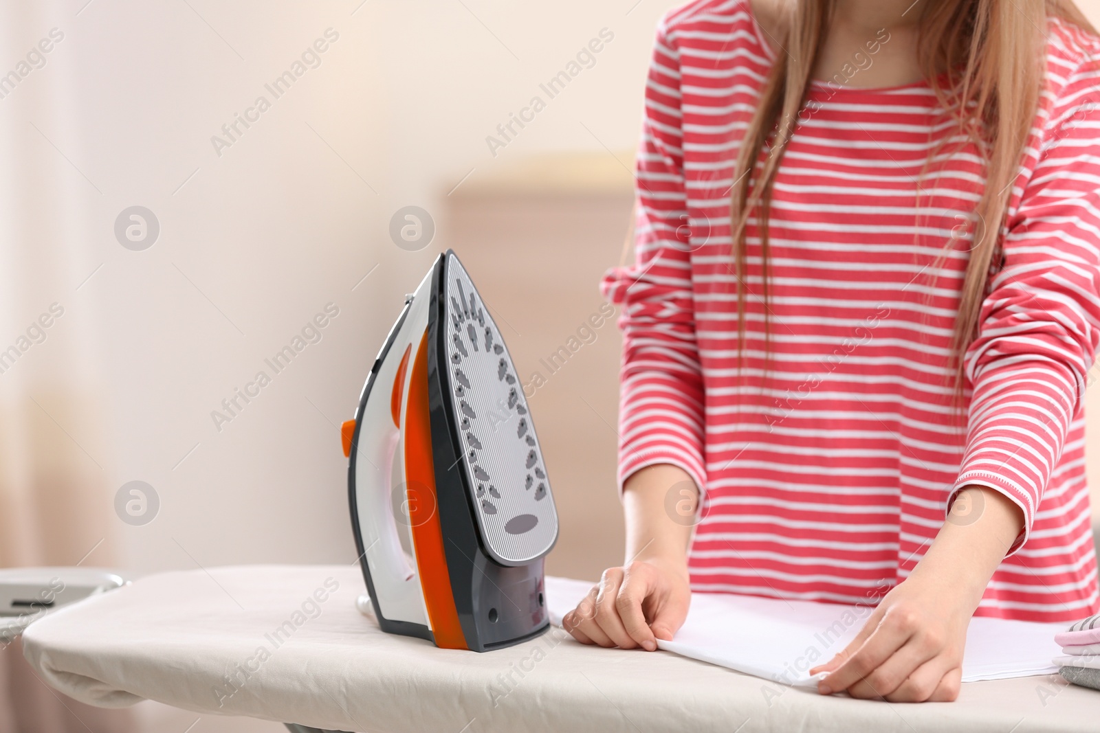 Photo of Young woman ironing clean laundry on board indoors, closeup