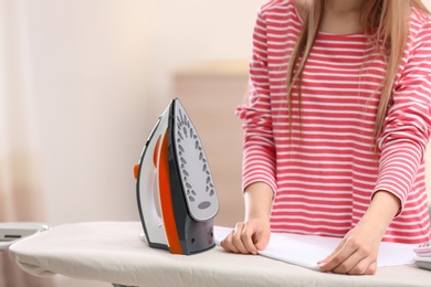 Young woman ironing clean laundry on board indoors, closeup