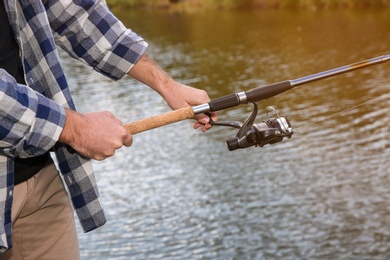 Photo of Man with rod fishing at riverside, focus on hands. Recreational activity