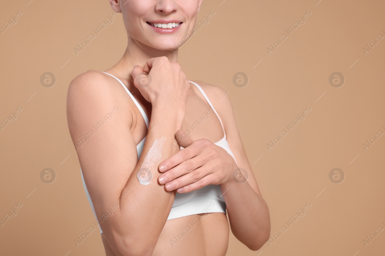 Photo of Woman applying body cream onto her arm against beige background, closeup. Space for text