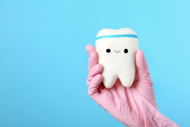 Photo of Dentist holding model of tooth with cute face on color background, space for text