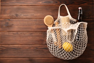 Photo of Fishnet bag with different items on wooden table, top view and space for text. Conscious consumption