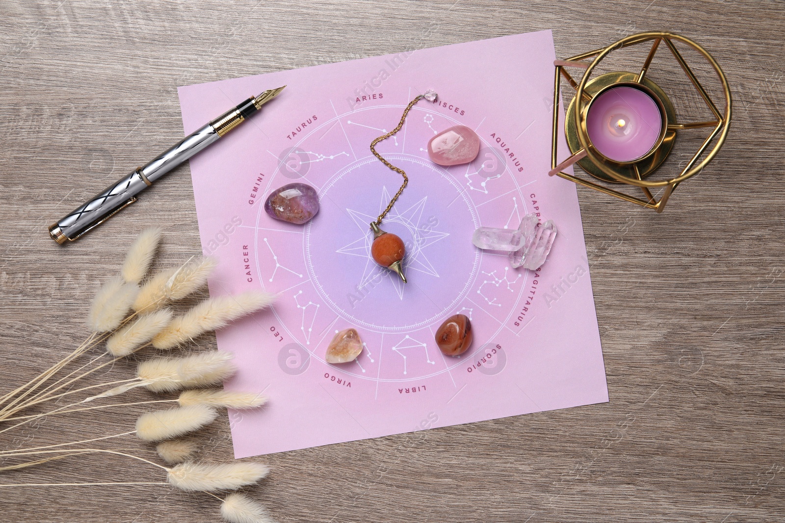 Photo of Astrology prediction. Zodiac wheel, gemstones, pendulum and burning candle on wooden table, flat lay